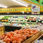 A grocery store produce section with crates of tomatoes, onions and citrus under a sign for farm fresh fruits and vegetables
