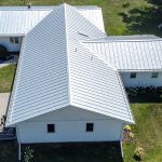 A white standing-seam metal roof on a small house with a lawn around it, seen from above