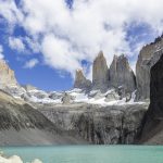 Granite peaks rising above a turquoise glacial lake under scattered clouds