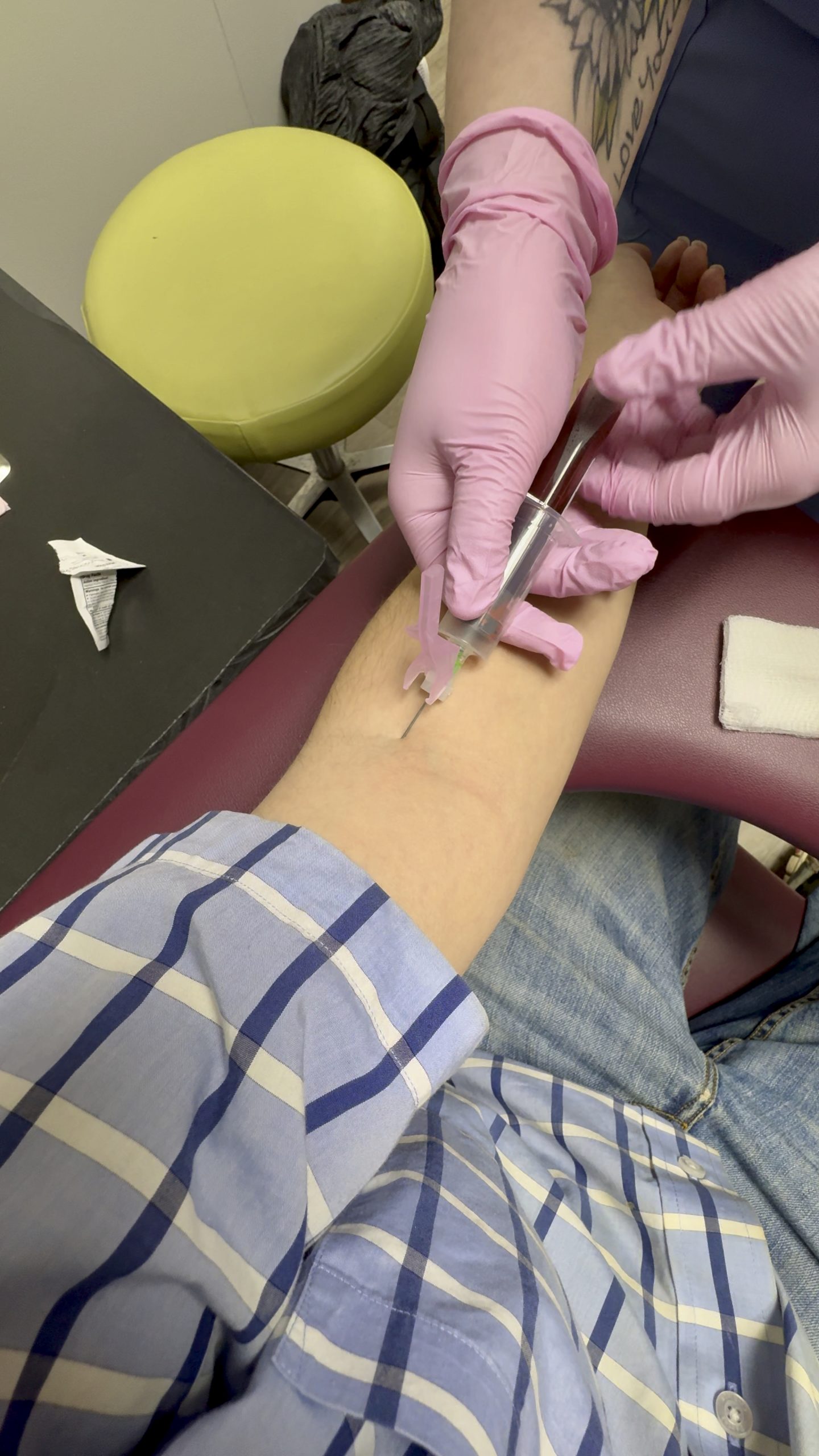 A gloved clinician draws blood from a patient's arm with a needle and collection tube.