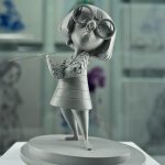 A gray sculpted figure of a small woman in oversized round glasses and a short bob on a round base
