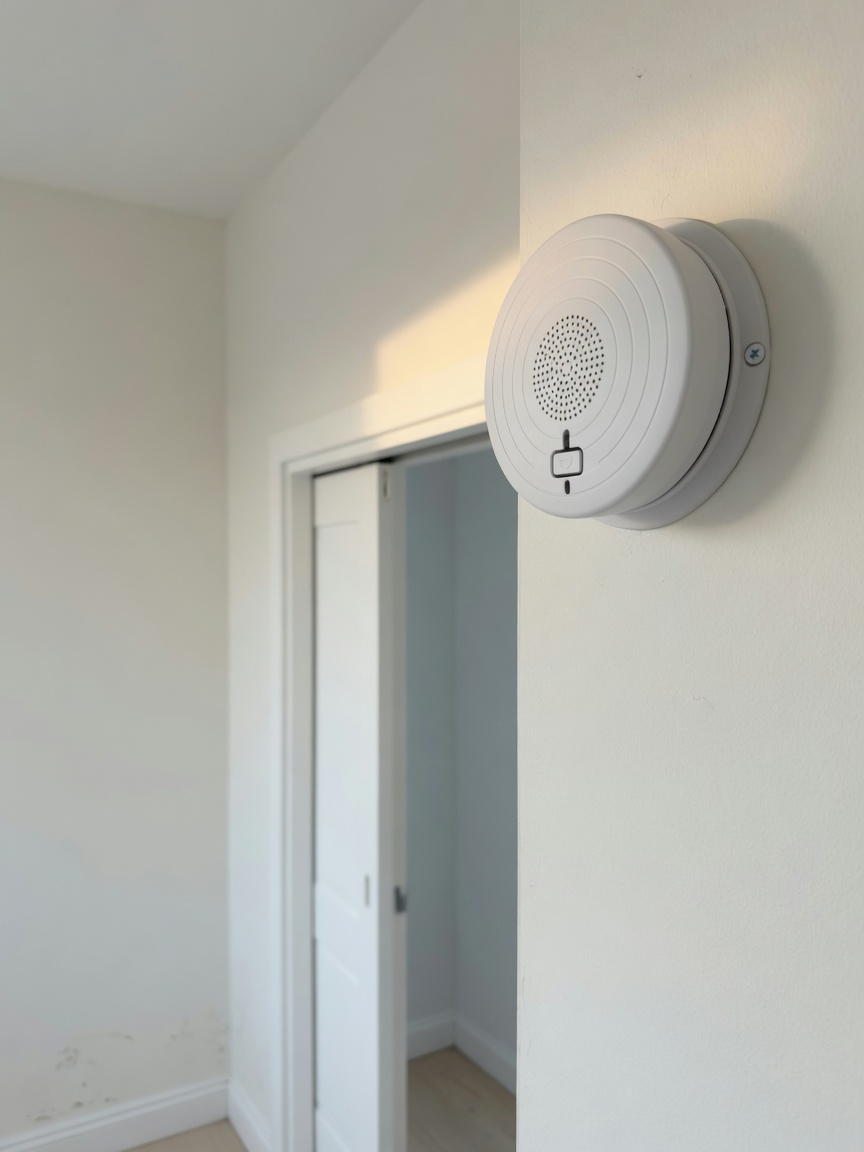 A carbon monoxide detector mounted on a wall near a bedroom doorway