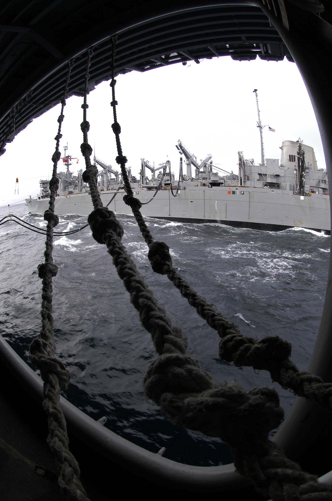 A Navy combat stores ship steams alongside USS Abraham Lincoln during an underway replenishment, transfer lines rigged between the two ships