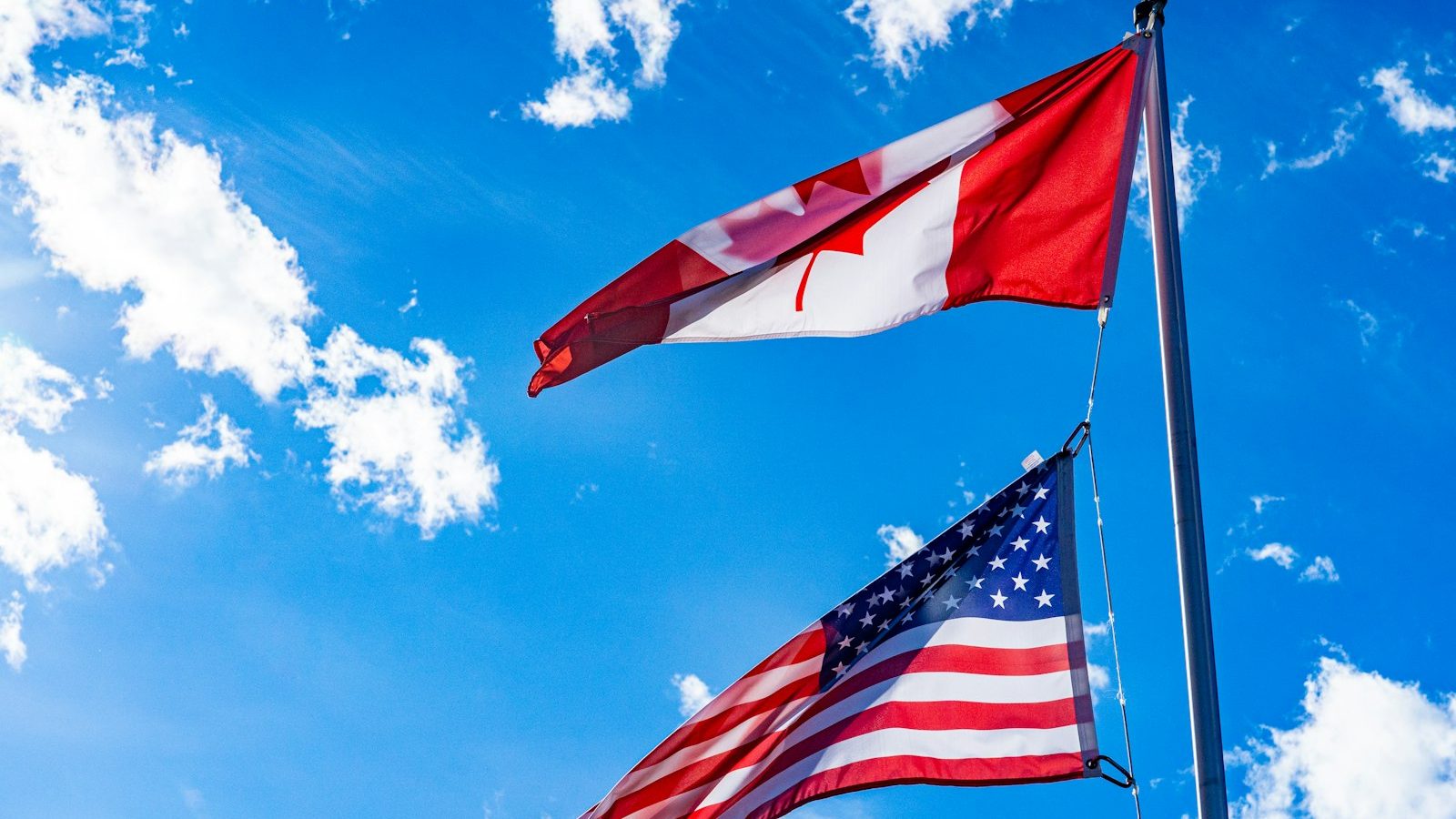 The American flag and the Canadian flag flying side by side in the wind.