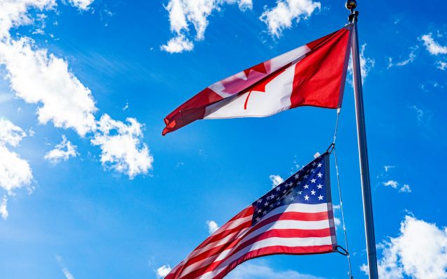 The American flag and the Canadian flag flying side by side in the wind.