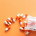 A single orange-and-white medication capsule on a plain white surface.