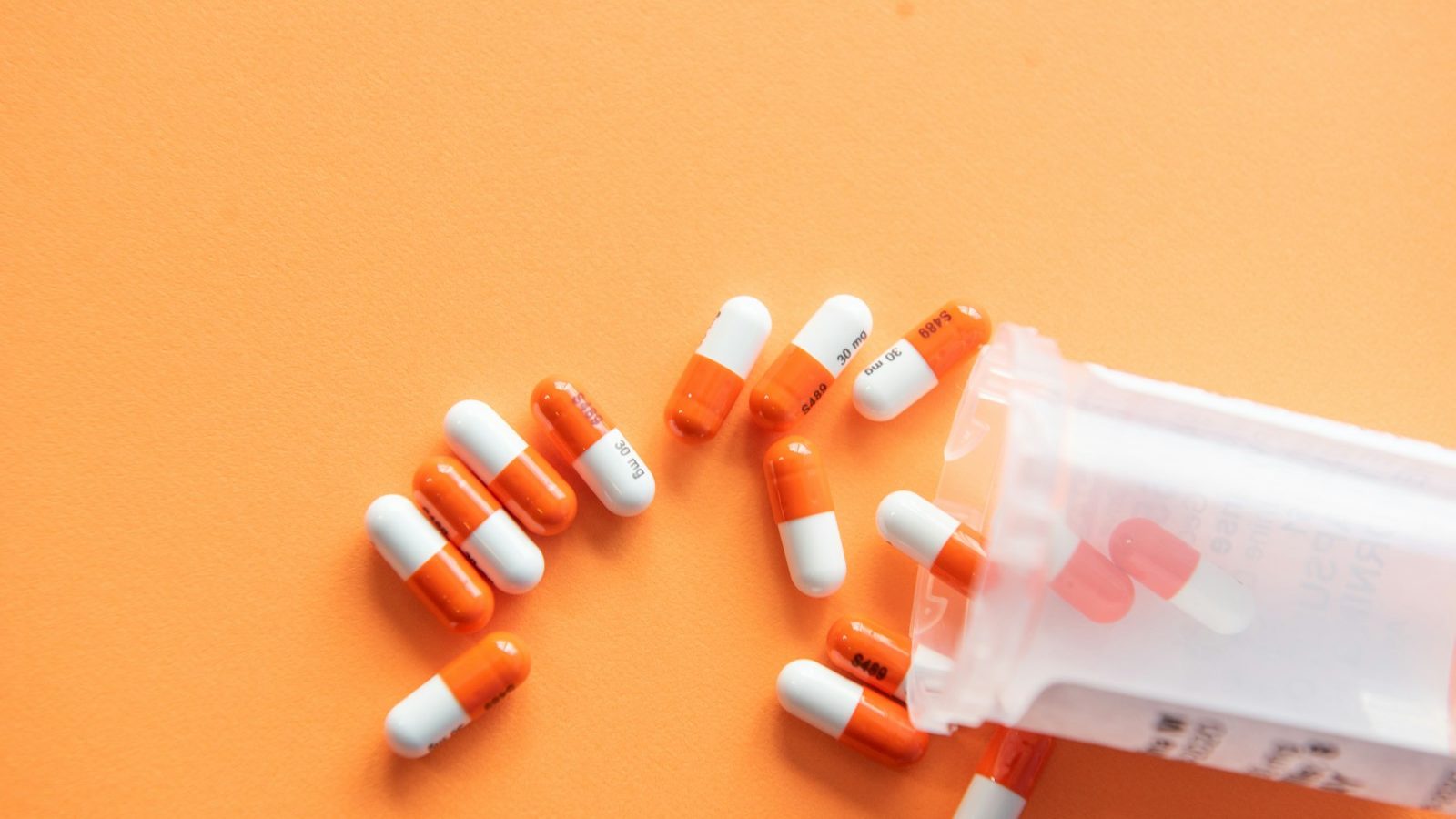A single orange-and-white medication capsule on a plain white surface.