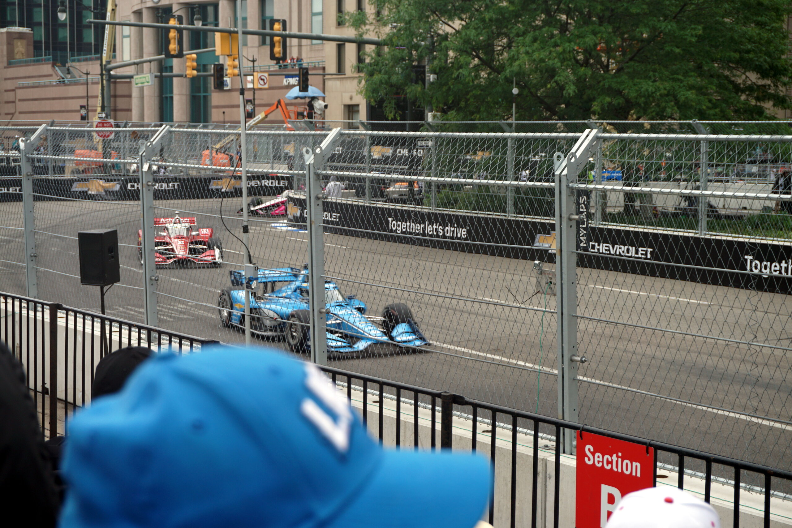 Two IndyCars round a downtown street-circuit corner lined with catch fencing and concrete barriers, city buildings behind.