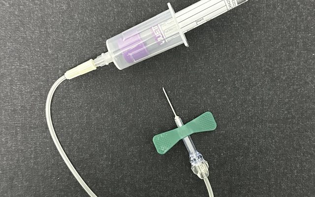 A capped blood-collection tube beside a butterfly needle and tubing laid out on a dark cloth.