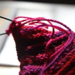Close-up of red yarn on circular knitting needles, a project in progress on a wooden table