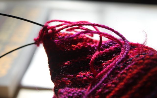 Close-up of red yarn on circular knitting needles, a project in progress on a wooden table