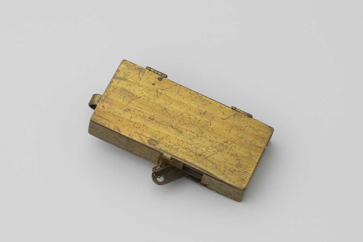 A worn brass mechanical pedometer, closed, resting on a plain background.