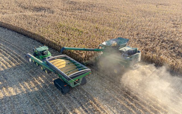 A combine unloads harvested corn into a grain cart in a field during harvest.