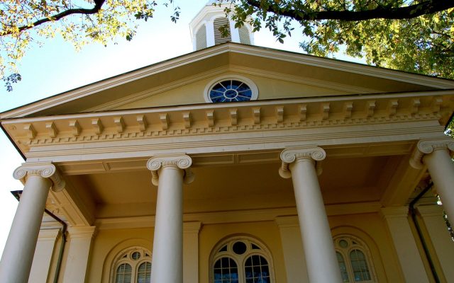 A red-brick county courthouse with white columns and a clock tower under a blue sky.