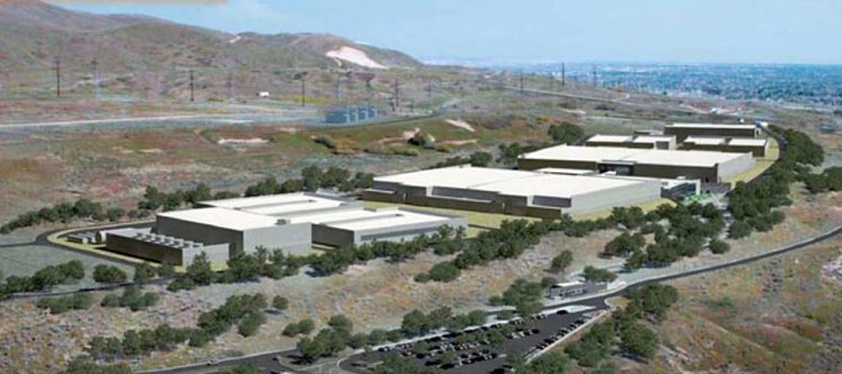 An aerial view of a sprawling data center complex with white roofs set in dry, tan desert terrain.