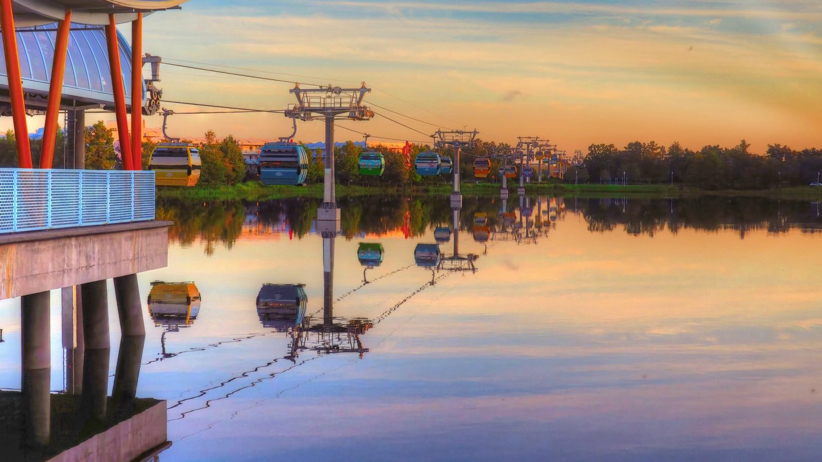 Colorful Disney Skyliner gondolas gliding over a still lake at dawn, mirrored in the water.