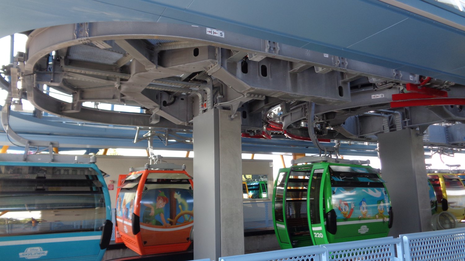 Rows of Disney Skyliner gondola cabins, wrapped in character art, waiting at a loading station.