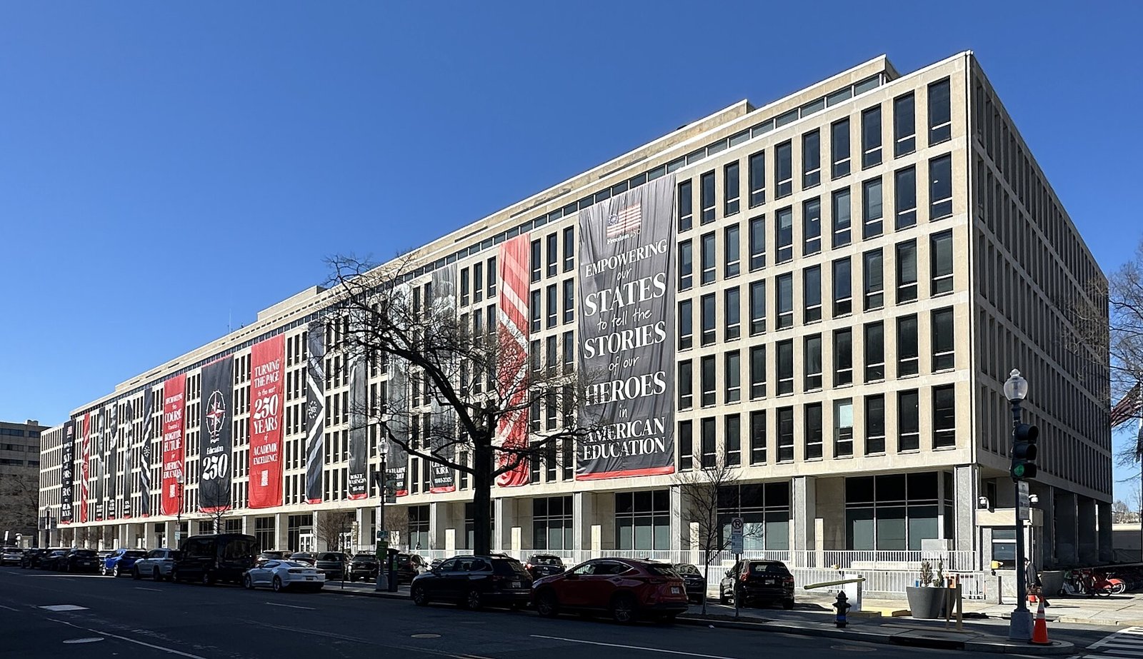 Large red, black and gray banners hang down the front of the Education Department headquarters building under a blue sky