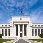 The marble facade of the Federal Reserve's headquarters in Washington under a blue sky.