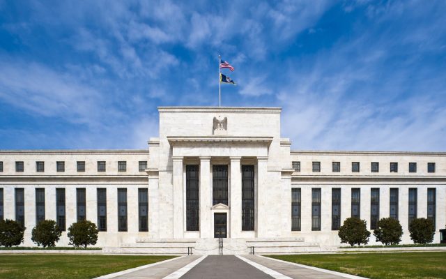 The marble facade of the Federal Reserve's headquarters in Washington under a blue sky.
