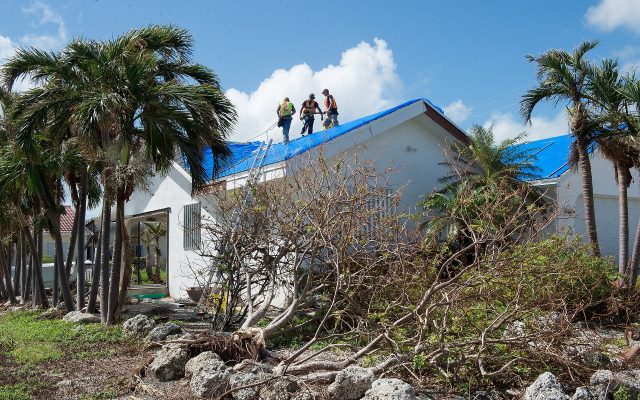 Workers install a blue tarp on a Florida Keys roof damaged by Hurricane Irma