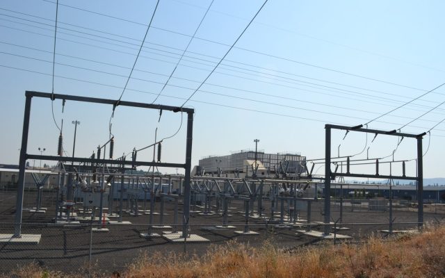 A low industrial data center building behind a chain-link fence on a bluff above the Columbia River at The Dalles, Oregon.