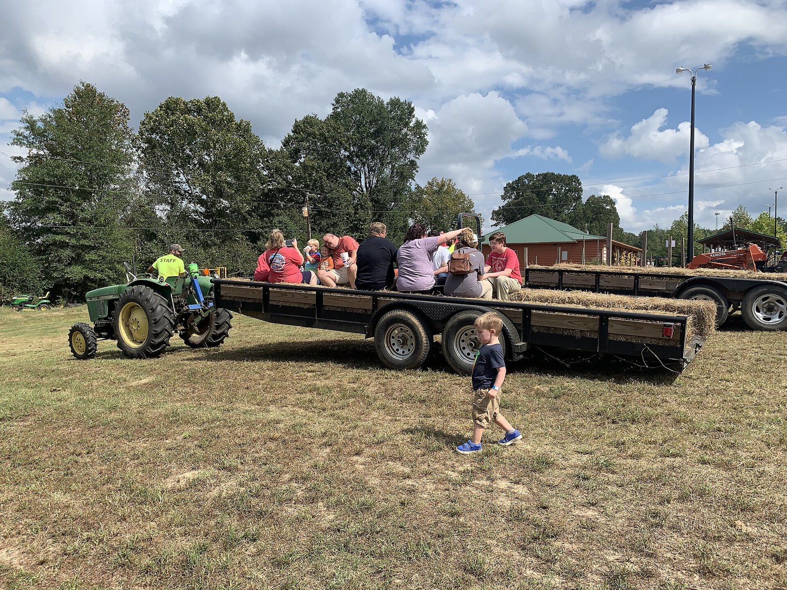 A green tractor pulling a hay wagon full of families across a grassy field