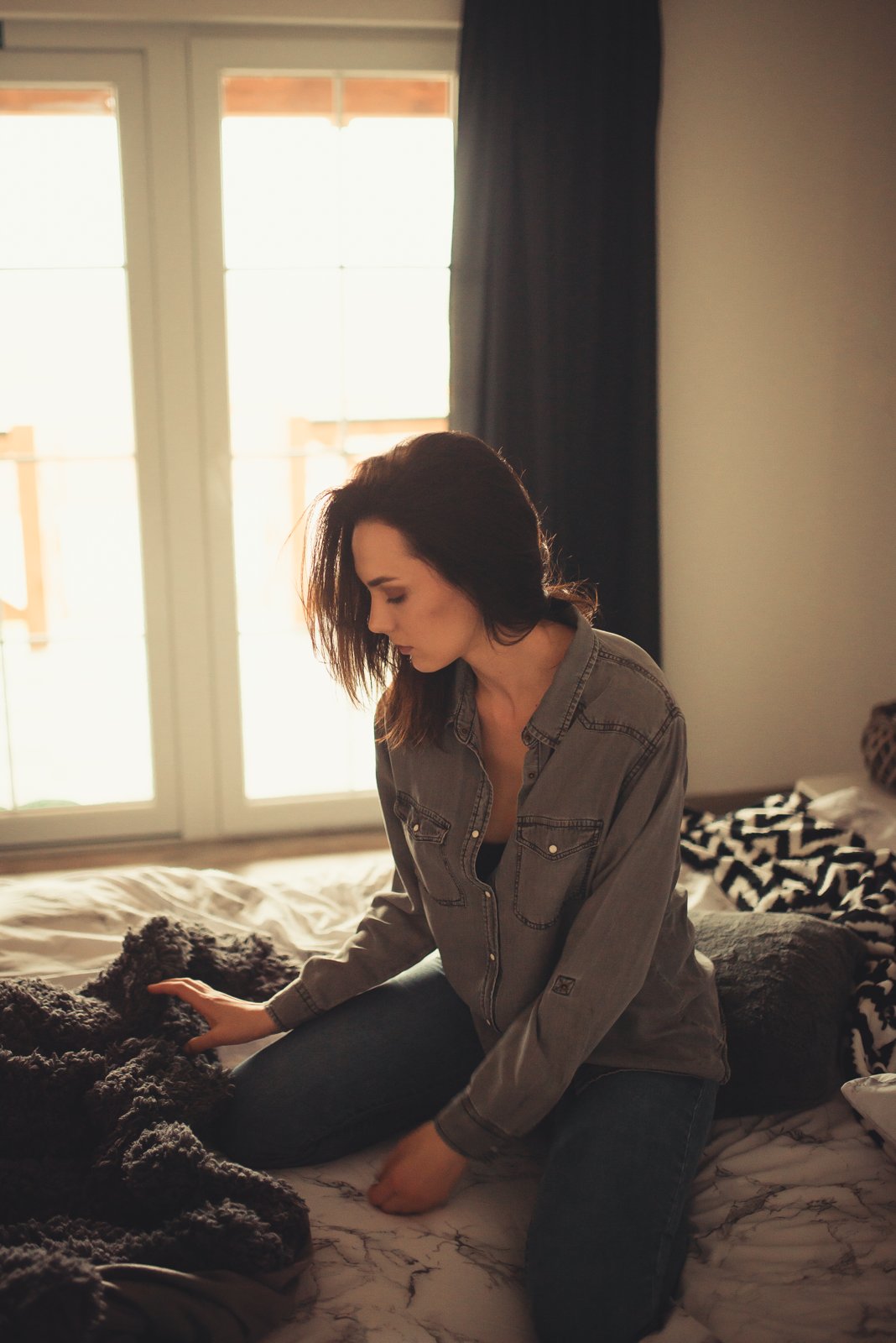 A person kneeling on a bed in the warm light of a window on a winter morning.