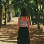 A woman walks away down a sunlit, tree-lined path.