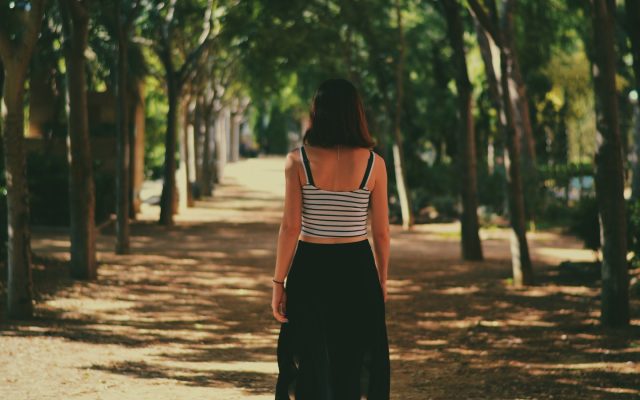A woman walks away down a sunlit, tree-lined path.