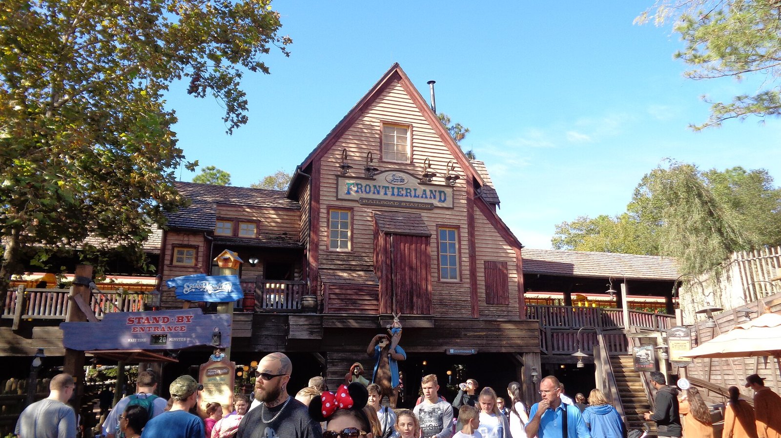 The red wooden Frontierland Railroad Station at Magic Kingdom with a Splash Mountain sign and crowds of guests in front