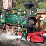 The green Lilly Belle steam locomotive of the Walt Disney World Railroad blowing steam beside a station and water tower at Magic Kingdom