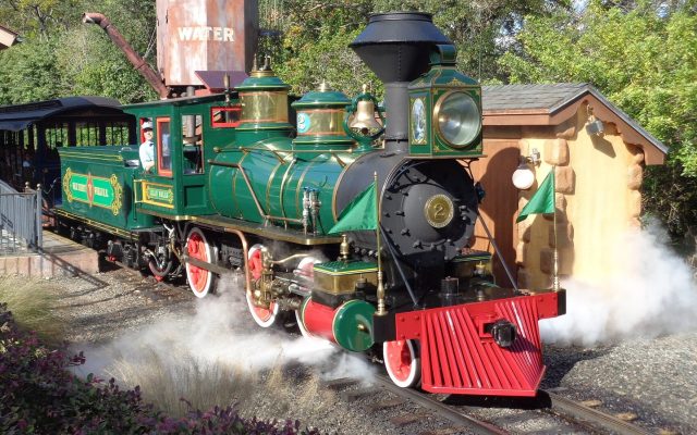 The green Lilly Belle steam locomotive of the Walt Disney World Railroad blowing steam beside a station and water tower at Magic Kingdom