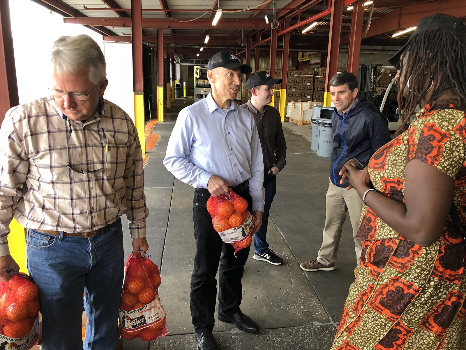 Visitors holding mesh bags of fresh oranges at a citrus packing house