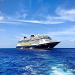 A large blue and white cruise ship with red funnels on open water under a blue sky