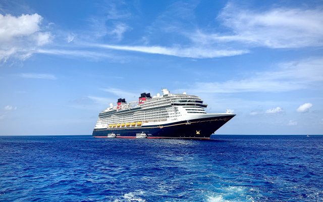 A large blue and white cruise ship with red funnels on open water under a blue sky