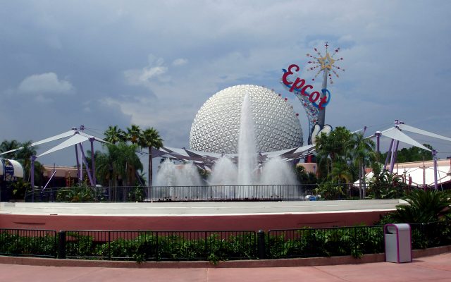 The silver geodesic sphere of Spaceship Earth behind a fountain and the Epcot sign on a cloudy day