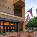The concrete facade of the J. Edgar Hoover Building with American flags and planters at dusk