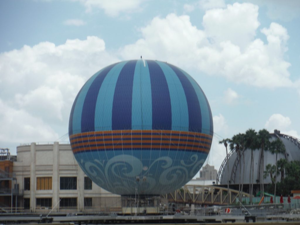 The striped blue and orange Aerophile balloon tethered above the West Side at Disney Springs under a cloudy sky