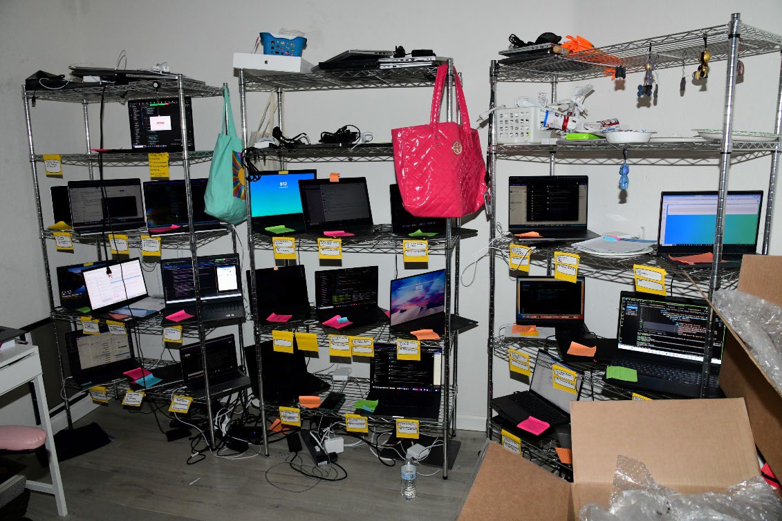 Metal shelving racks holding about two dozen laptops, each with a yellow sticky note, in a small room