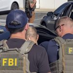 Two FBI agents escort Greg Lui beside a car during his arrest in Los Angeles County.