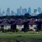 Rows of brick and tile-roofed houses in a Dallas suburb with the downtown Dallas skyline in the distance