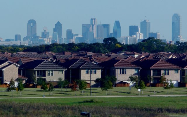 Rows of brick and tile-roofed houses in a Dallas suburb with the downtown Dallas skyline in the distance