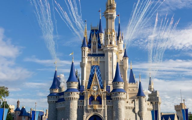 Cinderella Castle framed by daytime fireworks as Disney characters and guests gather in front.