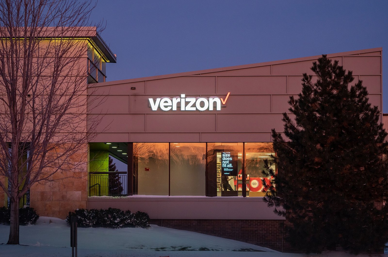 A Verizon store with a lit Verizon sign at dusk in the snow